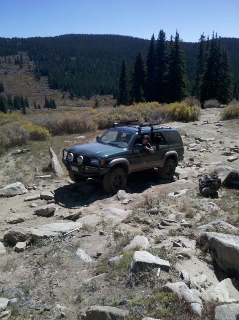 1996 Ford Bronco - A green SUV navigates a challenging rocky path in a mountainous, wooded area.
