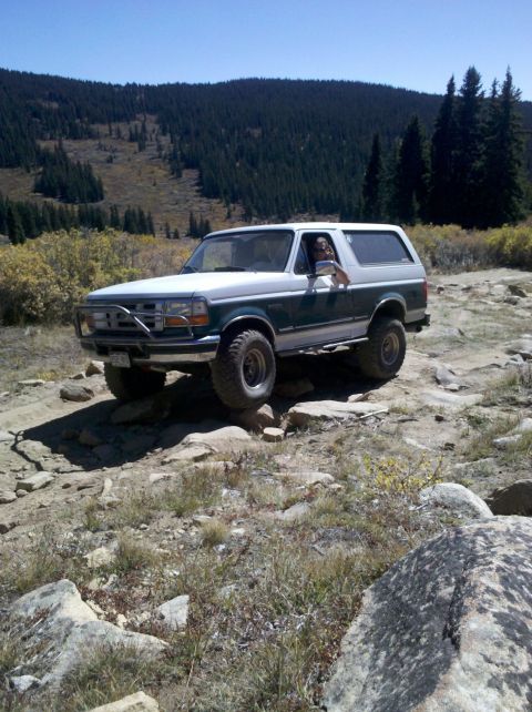 1996 Ford Bronco - A two-tone 1996 Ford Bronco navigates a , rocky mountain path under a clear blue sky.