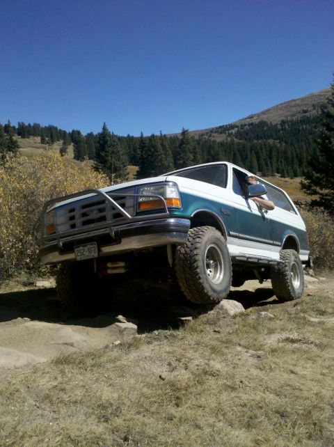 1996 Ford Bronco - A Ford Bronco navigates a rocky off-road trail under a clear blue sky.