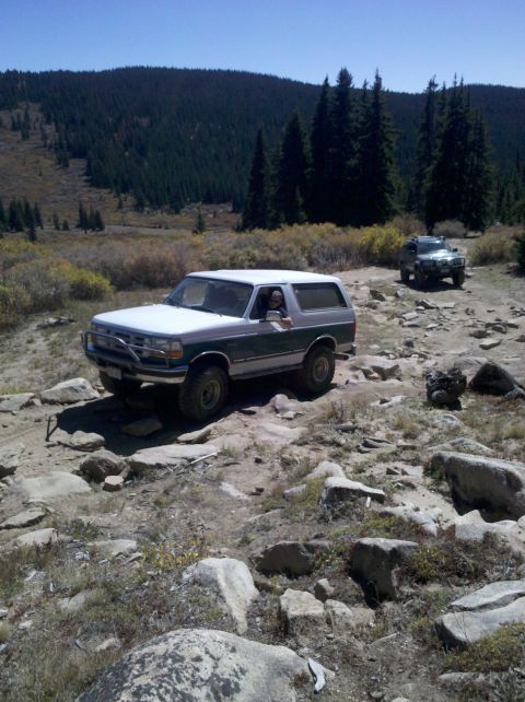 1996 Ford Bronco - A two-tone Ford Bronco navigates a rough, rocky terrain with a second SUV following behind.
