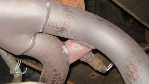 1988 Ford Bronco - The underside of a vehicle shows an exhaust pipe and an oxygen sensor, indicating a part of the emissions system.
