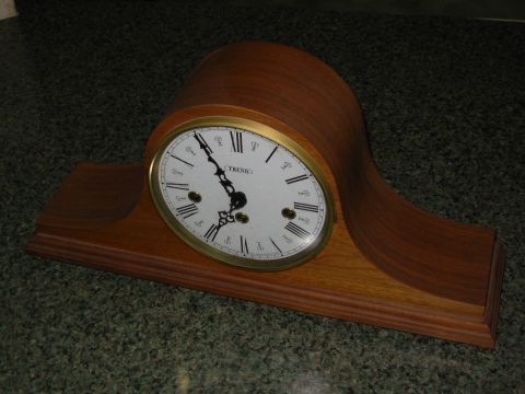 2004 Land Rover Land Rover - A wooden mantel clock with a white face, Roman numerals, and brass accents is displayed on a speckled surface.