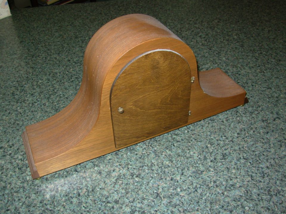 Wooden tambour mantel clock case seen from the rear with arched door on a green counter