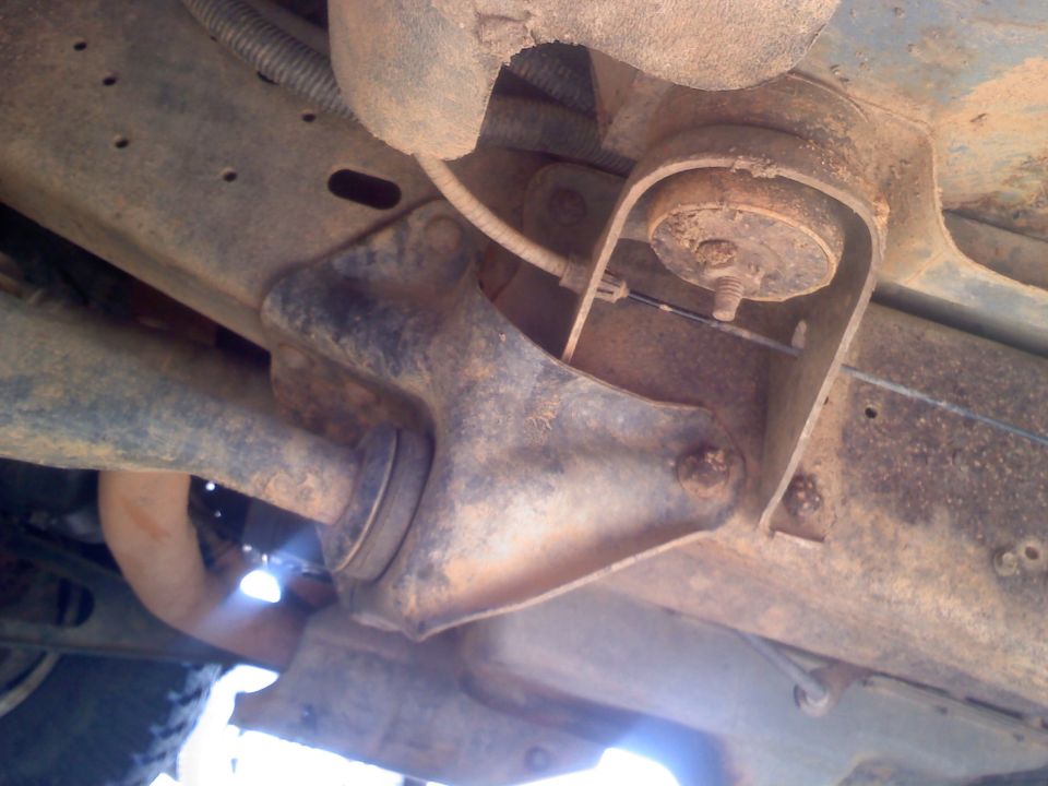 Underside view of rusty vehicle suspension parts, including a bracket and a shock absorber mount