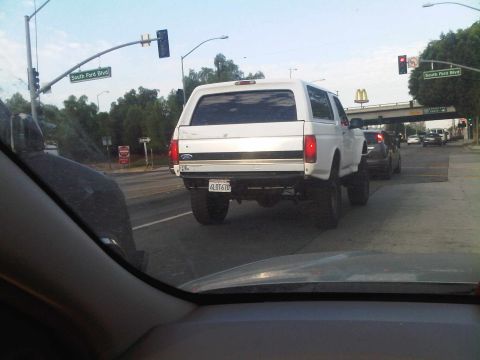 1986 Ford Bronco - A white Ford Bronco with a camper shell is seen from behind in traffic.