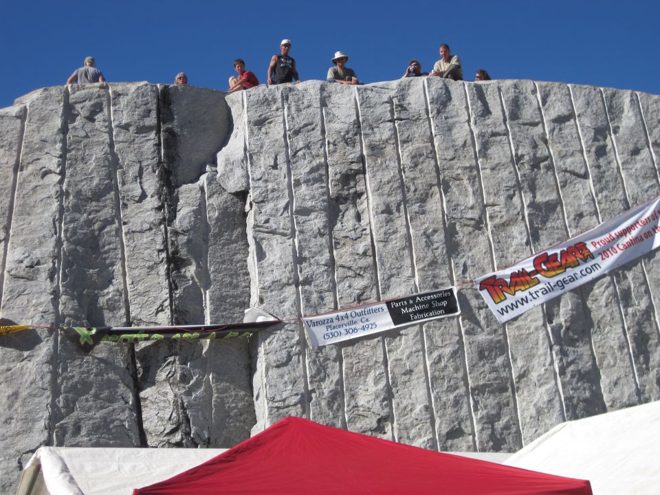 People stand atop a large, carved stone wall; banners hang on the wall