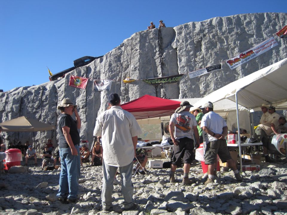Off-road vehicles on a rocky cliff face with tents and people below