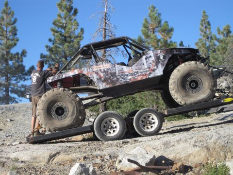 1989 Ford Bronco - A custom-built off-road buggy is loaded onto a trailer in a rocky, wooded area.
