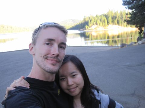 1989 Ford Bronco - A couple takes a selfie by a calm lake surrounded by pine trees.
