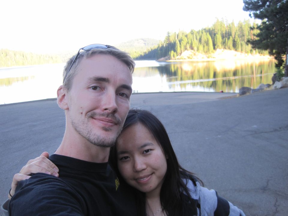 Couple posing for a selfie with a lake and trees in the background