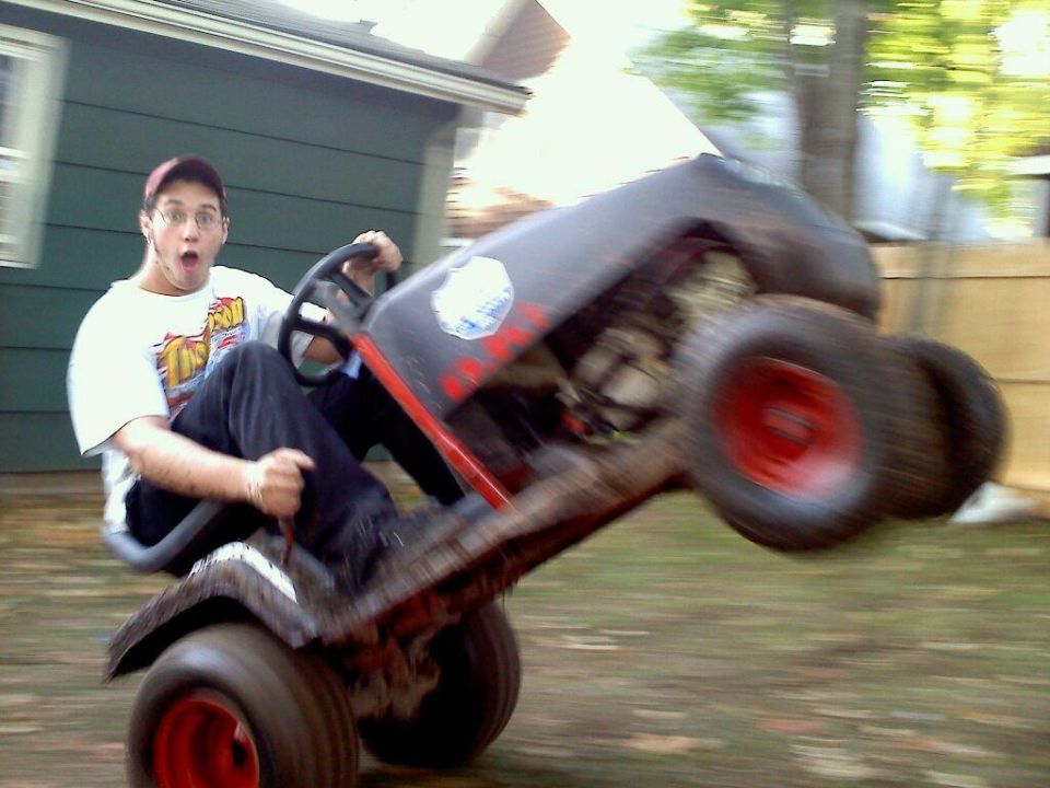 Person riding a riding lawn mower on two wheels, with a surprised expression