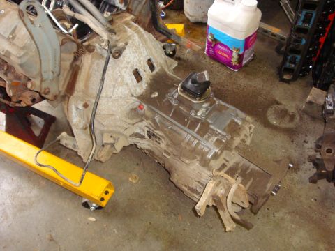 1989 Ford Bronco - Engine and transmission parts are laid out on the floor, with a yellow engine hoist arm providing support.