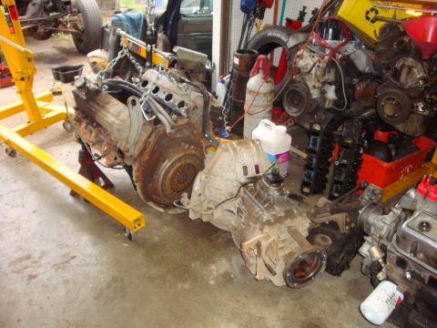 1989 Ford Bronco - Multiple vehicle engines and transmissions are disassembled and stored in a cluttered garage setting.