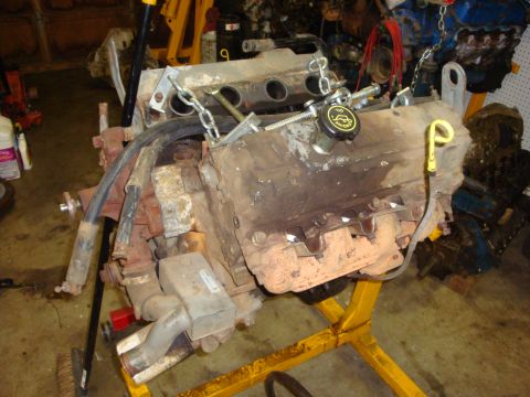 1989 Ford Bronco - An engine is mounted on a yellow stand in a workshop setting, with other engine parts visible in the background.