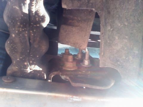 1996 Ford Bronco - Close-up underhood/undercarriage shot of a heavily surface-rusted bracket and welded mount, with rusty hex bolts and a nut threaded through…