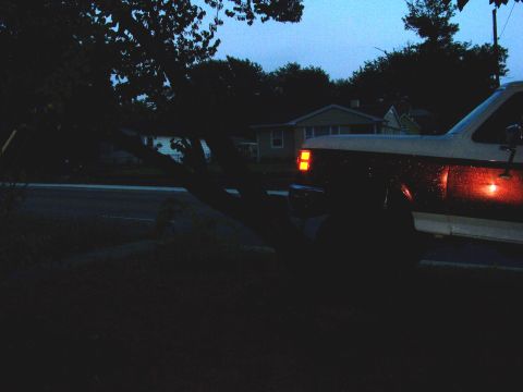 1989 Ford Bronco - A white and brown truck is seen at dusk, its amber turn signal and red brake light illuminated. The vehicle's body style suggests it is a 1…