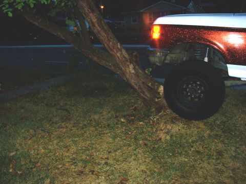 1989 Ford Bronco - Front corner of a 1992 Ford Bronco, showing the headlight and tire, parked near a tree at night.