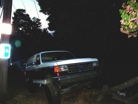 1989 Ford Bronco - This SUV is positioned precariously on a fallen tree trunk at dusk.
