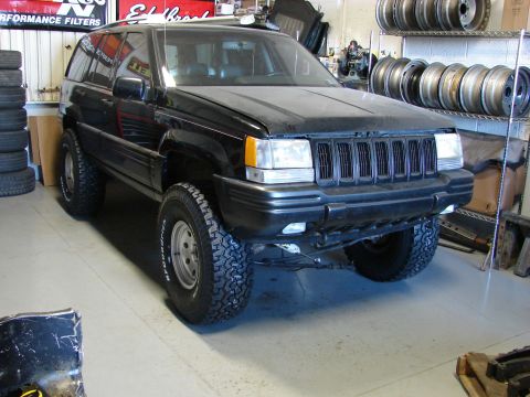 1996 Jeep Grand Cherokee - Black 1996 Jeep Grand Cherokee in a garage, showing its front 3/4 view with upgraded wheels.