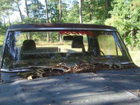 1986 Ford Bronco - This weathered truck, seen from the front, features a "Redneck" sticker on its windshield and appears to be in a state of disrepair.