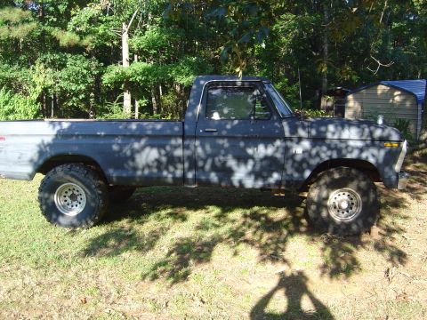 1986 Ford Bronco - Lifted Ford F-Series pickup truck parked on grass with trees in the background.