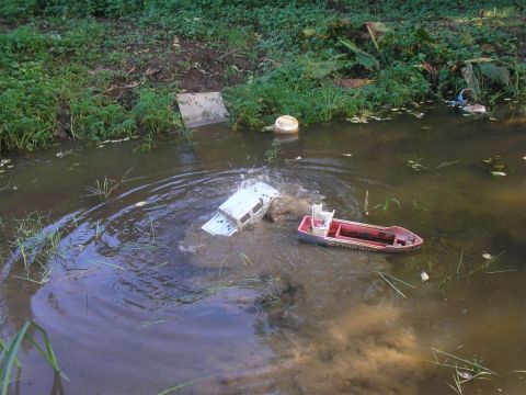 1994 Ford Escort - A toy SUV is partially submerged in muddy water, with a toy boat nearby.