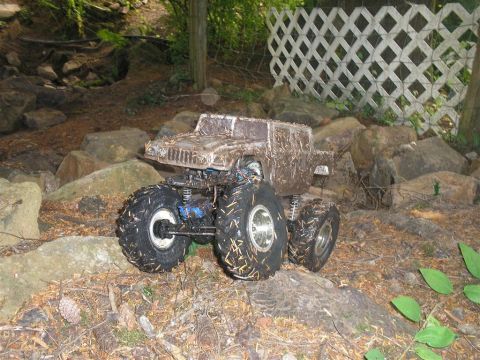 1994 Ford Escort - This remote control monster truck is covered in mud and appears to be navigating a rough outdoor terrain.