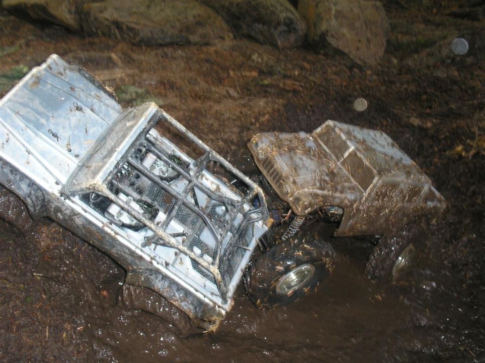 two RC trucks stuck in mud, one silver with a roll cage, the other brown