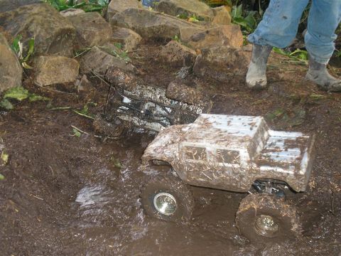 1994 Ford Escort - Remote control trucks are stuck in a muddy terrain with rocks and vegetation.