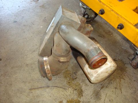 1989 Ford Bronco - A metal air intake component rests on a concrete floor near a yellow engine hoist.