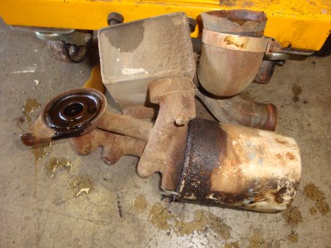 1989 Ford Bronco - Various rusty exhaust components are scattered on a concrete floor, some with visible oil stains.