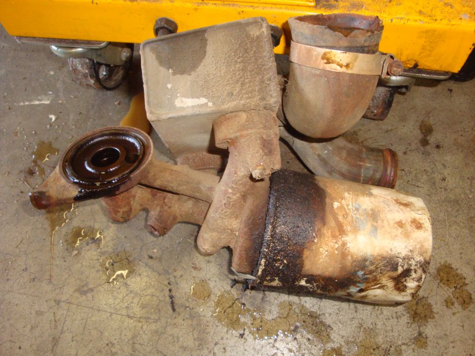 Rusty exhaust pipe and muffler parts with oil residue on a concrete floor