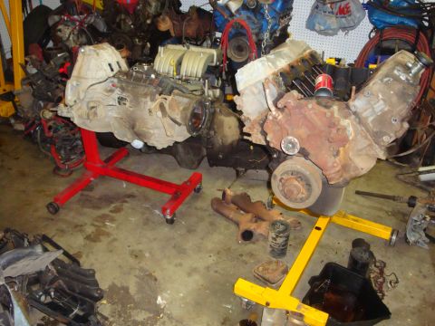 1989 Ford Bronco - Two engines are displayed on stands in a garage, surrounded by various automotive parts and equipment.