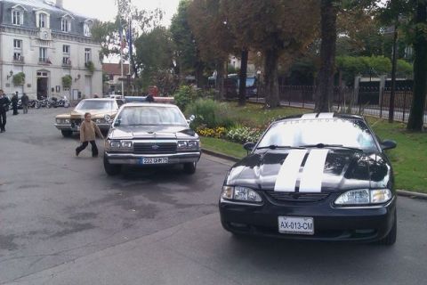 1991 Ford Crown Victoria - A black 1995 Ford Mustang with white stripes is parked in front of a police car.