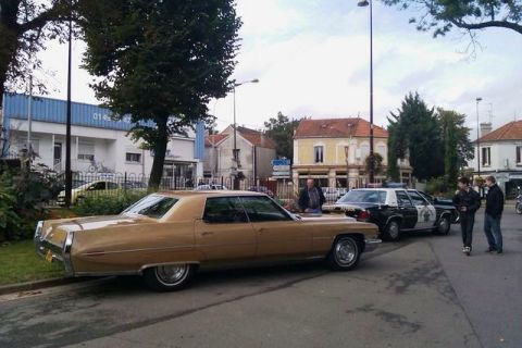 1991 Ford Crown Victoria - A vintage Cadillac and a police car are parked on a street with buildings in the background.