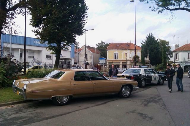 Tan 1970s Cadillac Coupe de Ville parked next to a police car
