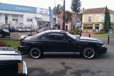 1991 Ford Crown Victoria - A black Ford Mustang coupe is parked on the street in front of a building.