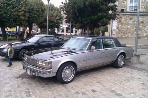 1991 Ford Crown Victoria - A 1980s Cadillac Seville and a black Ford Mustang are parked on a cobblestone street.