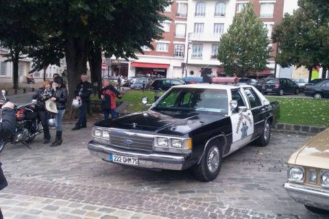 1991 Ford Crown Victoria - A 1991 Ford Crown Victoria police car is parked on a cobblestone street, with people and motorcycles nearby.