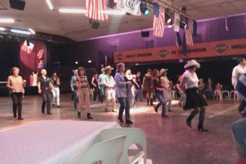 1991 Ford Crown Victoria - A group of people participate in line dancing at an indoor event with American flags and Harley-Davidson banners.