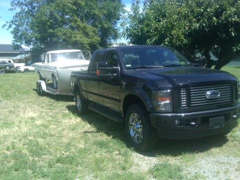 1988 Ford Bronco - A black Ford F-Series pickup truck tows a vintage pickup on a trailer.