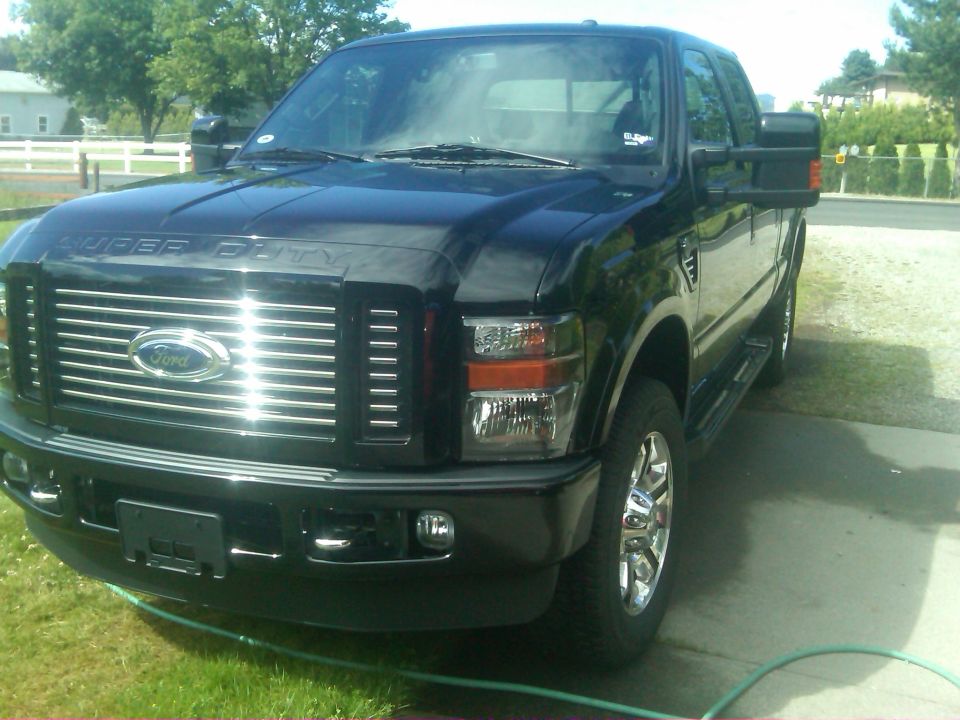 Black Ford Super Duty pickup truck parked on a driveway, front 3/4 view. "SUPER DUTY" is visible on the hood