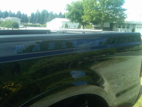 1988 Ford Bronco - The side of a black truck bed displays "HARLEY-DAVIDSON" lettering in blue, with reflections of the surrounding environment.