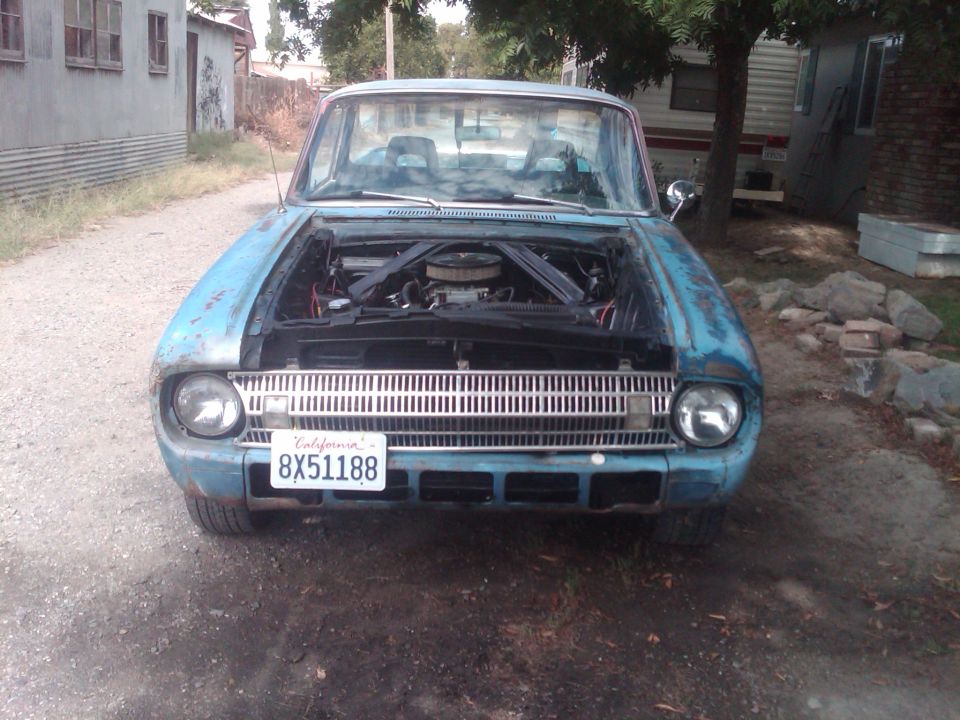 Front of light blue vintage Ford with hood off exposing V8 engine and chrome grille