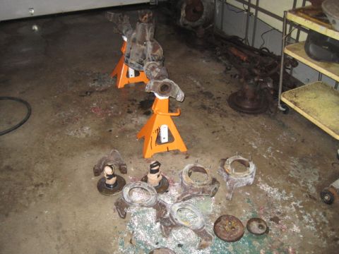 1979 Ford Bronco - Various vehicle suspension components, including axles and knuckles, are laid out on the floor and supported by orange jack stands.