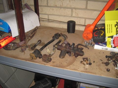 1979 Ford Bronco - Various rusty suspension parts and a steering gear box are laid out on a shelf.