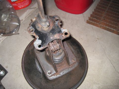 1979 Ford Bronco - Close-up of a rusty brake drum and associated suspension parts on a concrete floor.