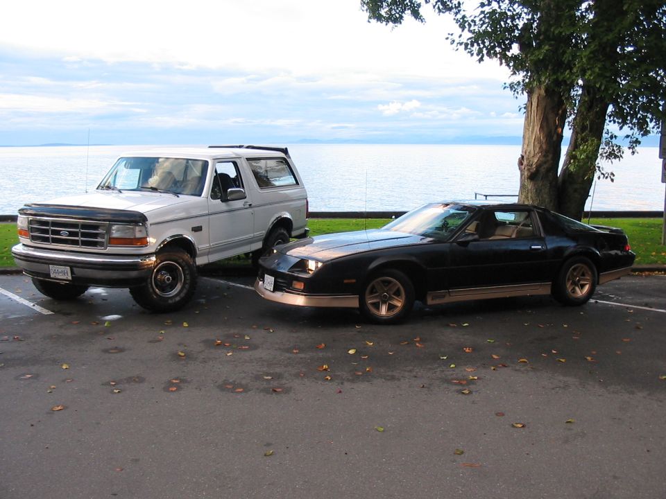 White 1992 Ford Bronco parked next to a black Chevrolet Camaro