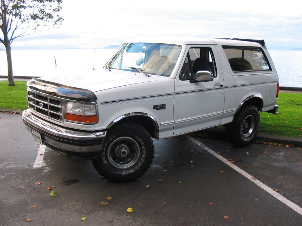 White 1995 Ford Bronco parked curbside with a water view