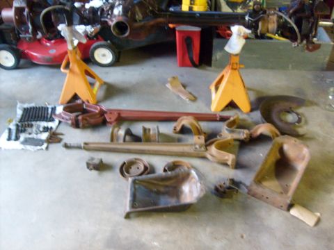 1986 Ford Bronco - Vehicle parts laid out on a floor next to a lawnmower and jack stands.